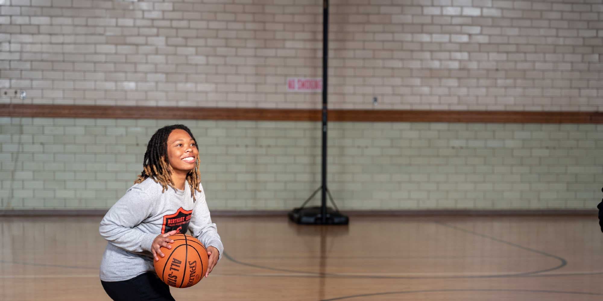 Smiling person holding a basketball in the Northeast Ohio College Preparatory School gym.