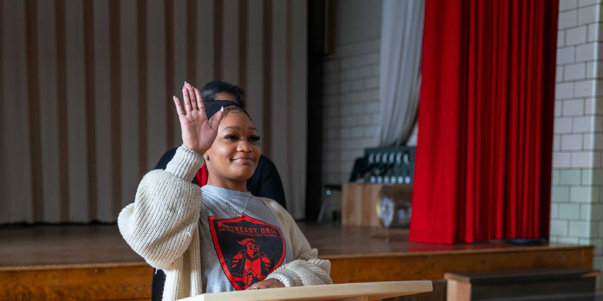 Adult raising a hand at a podium in front of a stage with red curtains.