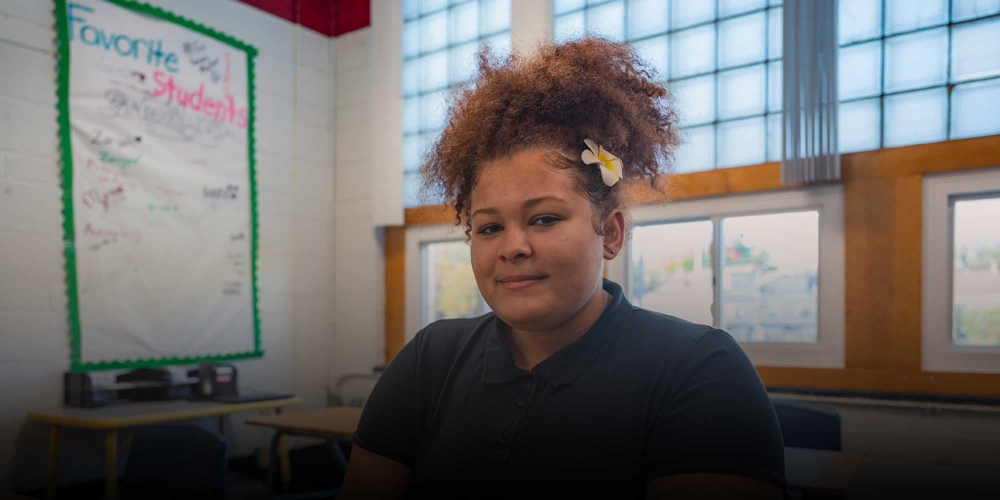 Student with a flower in their hair sitting in a classroom.