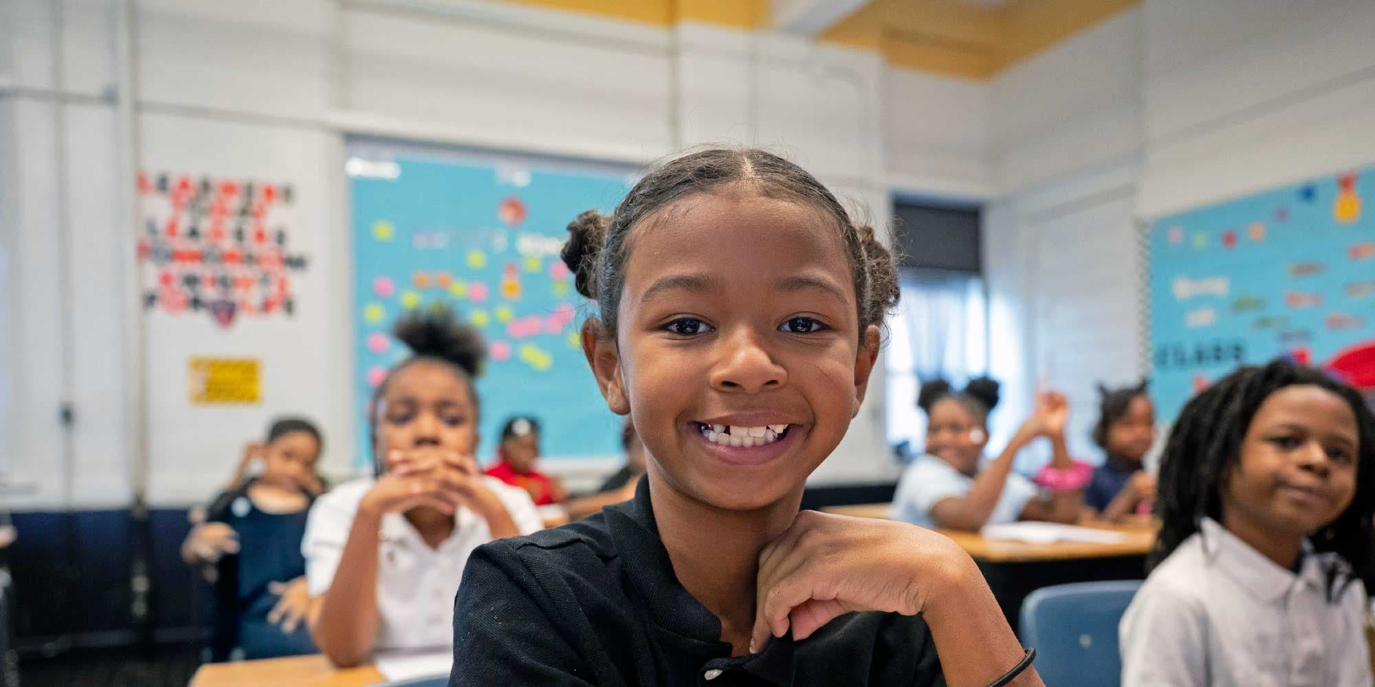 Smiling student with braided hair sitting at a classroom desk.
