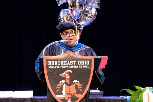 Adult in academic regalia speaking at a podium.
