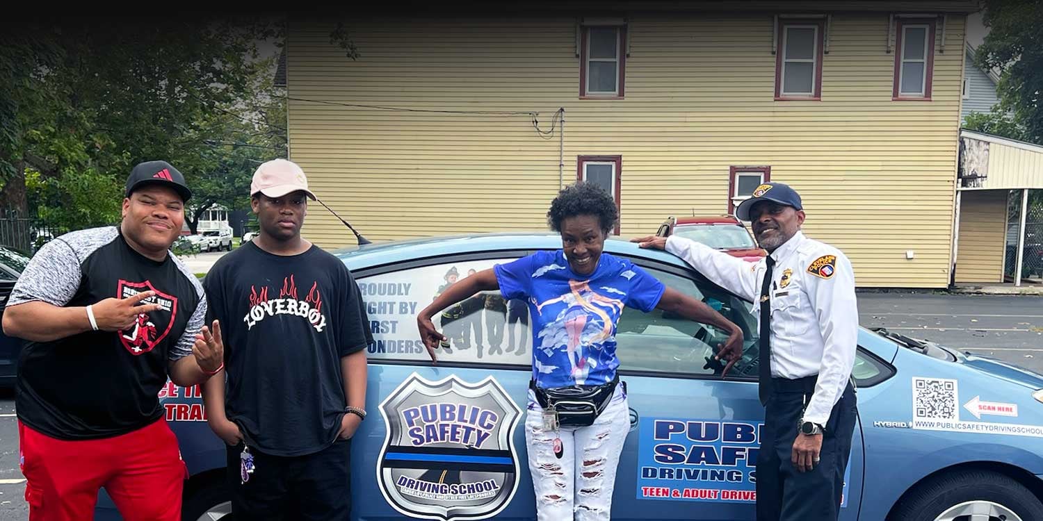 Four adults pose next to a blue driving school car.