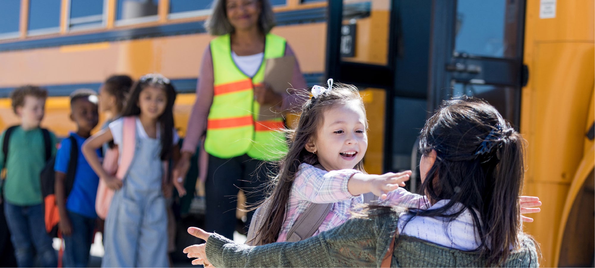 Child running to hug an adult near a school bus.