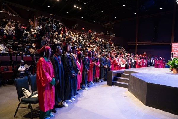 Adults in graduation caps and gowns on stage, facing an audience.