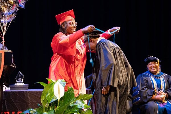 Adult in red gown placing stole on adult in black gown.